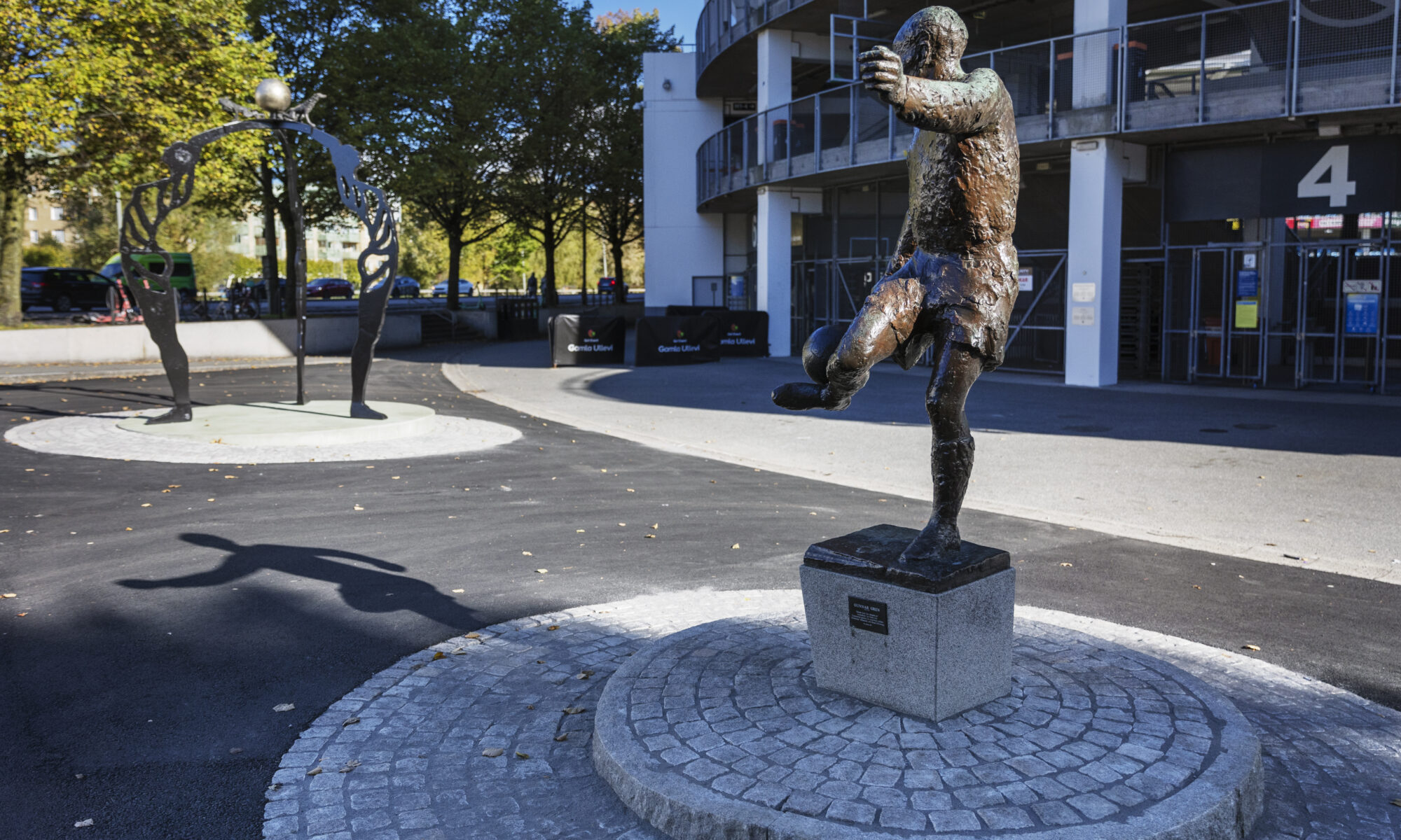 Ett foto av bronsskulptur av en man som kickar en boll, i bakgrunden en annan skulptur..